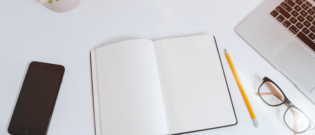 Picture of a desk with book, reading glasses, phone and laptop